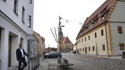 Bild: Petra Hartl
Hirschaus Bürgermeister Hermann Falk vor der neuen Ämter-„Außenstelle“ (links), gleich gegenüber des Rathauses (rechts). Dort ist jetzt das Erdgeschoss frei, damit kann die geplante Renovierung angepackt werden.