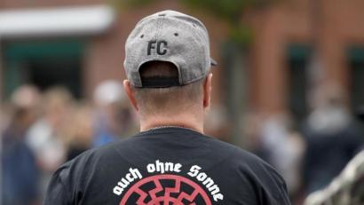 Bild: Caroline Seidel/dpa
Ein Teilnehmer einer rechten Kundgebung trägt ein T-Shirt mit einer Rune in Form einer halben "schwarzen Sonne" die einem Hakenkreuz ähnelt. Eine schwarze Sonne, Erkennungssymbol der rechtsextremen Szene, trägt CDU-Kreispolitiker Robert Möritz als Tattoo auf der Haut.