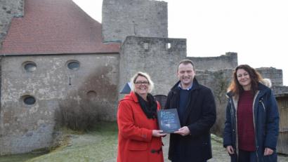 Bild: fz
Autorin Gabriele Kiesl (links) und Lektorin Manuela Bonfissuto (rechts) übergeben Bürgermeister Anton Kappl auf der Burg das Buch "Mystischen Burgen".