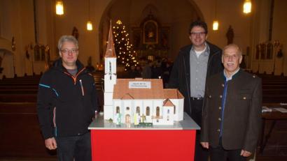 Bild: mmj
Pfarrer Wolfgang Dietz freute sich über das Engagement von Willibald Kulzer (links) und Hans Mösbauer (rechts), die eine Miniaturausgabe der Pfarrkirche im hinteren Teil des Kirchenschiffes aufstellten. Am Modell haben die Erbauer Fahnen mit den Farben der Stadt und der Kirche vor dem Eingangsportal gehisst.