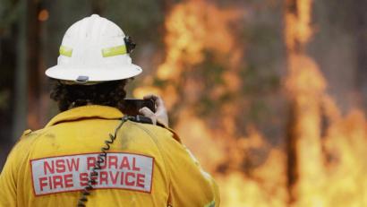 Symbolbild: Rick Rycroft/AP/dpa
Ein Feuerwehrmann im australischen New South Wales fotografiert mit seinem Smartphone eines der vielen Buschfeuer in der Region im Südosten des Landes.