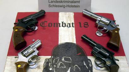 Archivbild: Horst Pfeiffer/dpa
Sichergestellte Waffen und ein Schild der kriminellen Neonazi-Gruppe "Combat 18" liegen im schleswig-holsteinischen Landeskriminalamt (LKA).