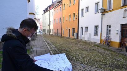 Bild: Hladik
Pfarrer Hans-Martin Meuß studiert den Plan. Der sieht vor, dass der Gehweg auf der Südseite von St. Michael (links zu sehen) verschwindet. Der Gehweg rechts entlang der Häuserzeile „Am Stock“ bleibt. Für die Anwohner werden – von der Schulgasse kommend – zwei Stellplätze zum Be- und Entladen eingerichtet.