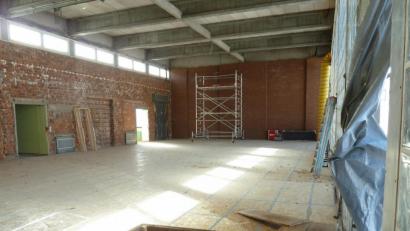 Bild: Portner
Die ehemalige Turnhalle präsentiert sich bereits als Rohbau. Der Schwingboden bleibt erhalten und ist mit USB-Platten abgedeckt, während die Holz-Deckenverkleidung abgebaut ist. Die Glasbausteinwand (rechts) wurde für eine Baustellentür geöffnet, welche Sturmtief „Sabine“ Anfang der Woche umlegte.