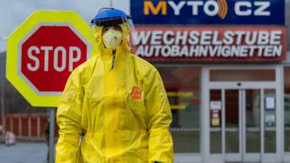 Bild: Robert Michael/dpa
Ein Feuerwehrmann steht in Schutzbekleidung während einer Kontrolle von Reisenden an einer Tankstelle.