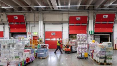 Bild: Peter Kneffel
Ein Mann schiebt eine mit Waren bepackten Palettenheber durch das Zentrallager REWE Süd. Foto: Peter Kneffel/dpa/Symbolbild