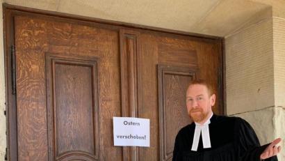 Bild: exb
Pfarrer Christoph Zeh steht vor verschlossenen Kirchentüren. Auf dem Schild ist "Ostern verschoben!" zu lesen.