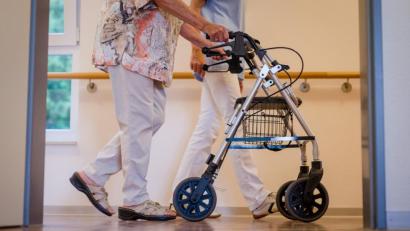 Bild: Christoph Schmidt
Eine Pflegekraft geht mit einer älteren Frau über einen Korridor in einem Pflegeheim. Viele Pflegekräfte erhalten nun einen Mindestlohn.