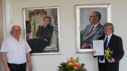 Bild: weu
Vor den Portraits des Ehepaars Max und Margret Schwarz, deren Vermächtnis im Arbeitsleben von Wolfgang Ruhland (rechts) eine tragende Rolle spielt, überreichte Bürgermeister Weigl die Urkunde zum Dienstjubiläum.