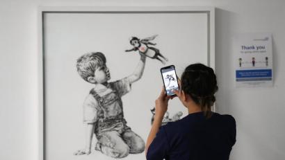 Bild: Andrew Matthews
Eine medizinische Mitarbeiterin fotografiert das Banksy-Kunstwerk mit dem Titel „Game Changer“. Foto: Andrew Matthews/PA Wire/dpa