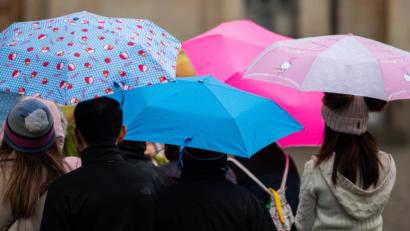 Symbolbild: Robert Michael/dpa
Menschen gehen mit Regenschirmen durch die Innenstadt.