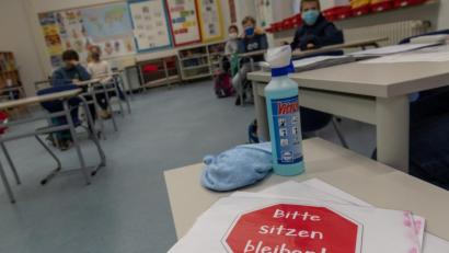 Bild: Peter Kneffel/dpa
Ein Schild mit der Aufschrift "Bitte sitzen bleiben!" liegt auf einem Tisch im Klassenraum einer vierten Klasse.