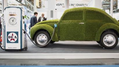 Bild: Julian Stratenschulte/dpa
Wie grün ist das E-Auto? Ein Ladekabel steckt in einem mit grünem Kunstrasen überzogenen VW Käfer.