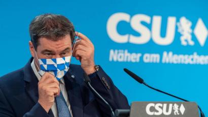 Bild: Peter Kneffel
Markus Söder (CSU) steht auf einem Podium und setzt sich seine Mundschutzmaske auf. Foto: Peter Kneffel/dpa