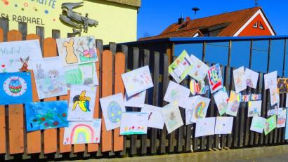 Bild: e
Am Außenzaun des Kindergartens St. Raphael in Kümmersbruck hängen Zeichnungen der Mädchen und Buben. Sie vermissen ihre Kita.