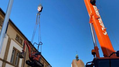 Bild: Stefanie Gradl
Hoch in den blauen Himmel schwebt der Minibagger, damit er über das Rathausdach in den Innenhof gelangen kann.