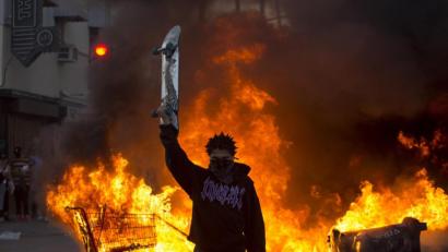 Bild: Ringo H.W. Chiu/dpa
Ein Demonstrant hält in Los Angeles ein Skateboard in die Höhe, während hinter ihm ein Einkaufswagen auf der Straße brennt.