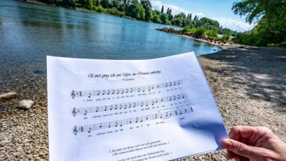 Bild: Armin Weigel
Ein Notenblatt mit dem Liedtext „Einst ging ich am Ufer der Donau entlang“ wird am Donauufer gehalten.