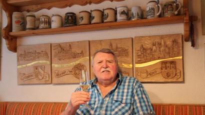 Bild: prh
Auch wenn die große Geburtstagsfeier momentan wegen der Corona-Krise auf Eis liegt. An seinem 70. Geburtstag erhob der Schnitzer, Musiker und Familienmensch Alfons Kistenpfennig trotzdem sein Glas vor seinen geschnitzten Relieffs mit den Stadtwappen und Silhouetten von Prag, Tachau, Neustadt und Nürnberg.
