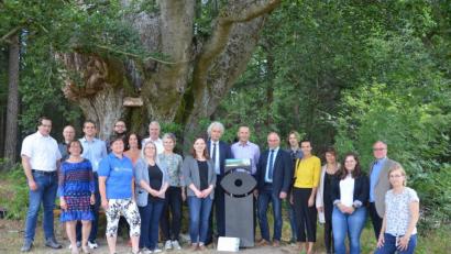 Bild: Benkhardt
Seltsame Stelen werden derzeit landauf, landab im Oberpfälzer Wald aufgestellt. Eine enthüllten stellvertretender Landrat Albert Nickl aus dem Landkreis Neustadt/WN, Walter Frank von der Firma Glapor aus Mitterteich und Landrat Wolfgang Lippert aus Tirschenreuth (Siebter bis Neunter von rechts) am Mittwoch unter der 350 Jahre alten Buche am Waldfriedhof Friedenfels.