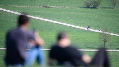 Bild: Sebastian Gollnow/dpa
Zwei Männer sitzen auf einem Hügel in der Sonne. Im Hintergrund gehen zwei Spaziergänger. In Thüringen werden die Kontaktbeschränkungen aufgehoben.