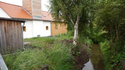 Bild: bkr
Am Erlenbach entlang, hinter dem Alten Feuerwehrhaus, soll ein Gehweg angelegt werden. Sträucher und Kräuter sollen ein Hineinrutschen von der Böschung und der Mauer verhindern. Die Mauer selbst beginnt dort, wo Büsche das Bachbett überdecken.