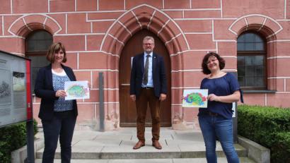 Bild: cog
Claudia Hammer, die Konrektorin der Pestalozzischule, (links) und Märchenerzählerin Tanja Weiß (rechts) präsentieren die ersten bunt ausgemaslten Bilder zum Märchen "Dort, wo der Drache wchläft". Bürgermeister Michael Göth (Mitte) dankt ihnen für ihr Engagement.