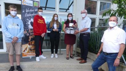 Bild: rn
Im Beisein von stellvertretendem Schulleiter Bernhard Miedl übergaben Walter Schnoy und Annegret Kennel an die Absolventen Annalena Walter (10c), Andre Andrigo und Luis Lottes (beide 10d) Mund- und Nasenmasken mit dem Schriftzug ihrer Schule.