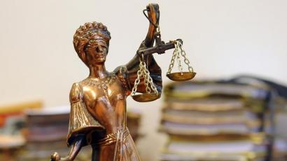 Symbolbild: Britta Pedersen
Eine goldfarbene Justitia-Figur steht vor Aktenbergen.