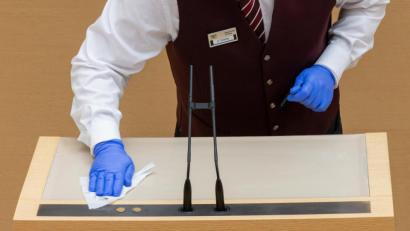 Bild:  Peter Kneffel/dpa
Ein Mitarbeiter des Landtags desinfiziert während der Plenarsitzung des bayerischen Landtags das Rednerpult.