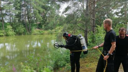Bild: wpt
Der Taucher der Bereitschaftspolizei ist kurz davor, den kleineren der beiden Weiher in der Nähe des Tatorts in Büchelkühn, nach der Tatwaffe abzusuchen.Seine Kollegen sichern ihn.