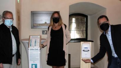 Bild: wro
Im Mittelpunkt steht die Gesundheit der Gäste und der Mitarbeiter. Im Eingangsbereich der Burg Falkenberg fallen Hinweise auf das Hygienekonzept und ein Desinfektionsmittel-Spender auf. Gerhard Pöschl, Teresa Würth und Matthias Grundler (von links) informierten über Details.