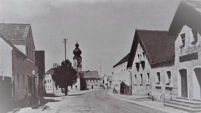 Bild: exb
Die Aufnahme von 1937 zeigt die Kirche nach dem Brand mit dem neuen Turm und am Tillyplatz auf der linken Seite die Tankstelle und das Geschäftshaus Müller (Waldmüller) und rechts die Anwesen Lang (Alisn), Wild (Gougl) und Meckl (Pöiterlsimmer).