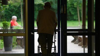 Symbolbild: Peter Steffen
Ein Senior geht mit einer Gehilfe durch eine Tür in einem Altenheim.