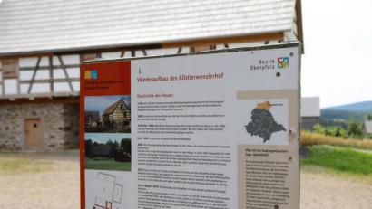 Bild: Gerhard Götz
Auf der Fläche zwischen der Infotafel, auf der der Köstlerwenzlhof unter dem Namen Köstlerwenzlerhof geführt wird, und dem Gebäude im Hintergrund entsteht das neue Bauernhaus.