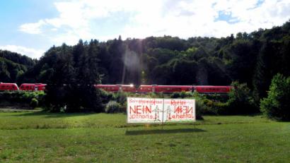 Bild: Stephan Huber
„Bahnstromtrasse Nein – Rettet das Lehental“ steht auf Transparenten, die Bürger an mehreren Stellen rund um Oed (Weigendorf) aufgestellt haben. Dahinter fährt ein dieselbetriebener Regionalexpress der Bahn. Um die Züge mit Strom zu betreiben, will die Bahn eine Stromtrasse in die teils geschützte, naturbelassene Landschaft bauen.