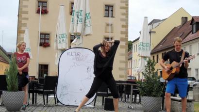 Bild: mor
Die „Hexe von Obermenzing“, lautet der Titel des Märchentanzes, den Lea Kopff zusammen mit Collin Willhauk (Gitarre) und Kim Mira Meyer (Gesang) beim Spontankonzert von „Kultur auf Rädern“ auf dem Pflaster vor dem Rathaus präsentiert.