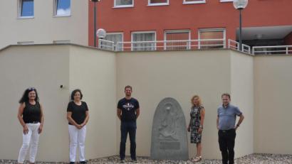 Bild: dob
Der heimische Granitstein zeigt ein Werk der Barmherzigkeit. Ein Steinmetz hat diese Darstellung im frühen 19. Jahrhundert akribisch aus dem Stein herausgearbeitet. Christine Schmidt (Zweite von rechts) vermachte das Kunstwerk nun der katholischen Pfarrgemeinde. Die Aufstellung war ein Gemeinschaftswerk von Schmidt und Bauunternehmer Michael Töppel (Dritter von links), der seine Fundamentarbeiten ebenfalls kostenlos einbrachte. Die Vertreterinnen des Walter-Siegert-Caritasheims Karin Witt und Johanna Bodensteiner (von links) waren ebenfalls angetan von diesen Spenden.