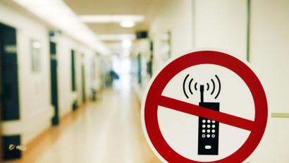 Symbolbild: Sebastian Widmann/dpa
Ein Handy-Verbotsschild klebt an der Glastür eines Krankenhauses. In den meisten Bereichen darf trotzdem telefoniert werden, doch Patienten müssen in ländlichen Regionen auch mal damit rechnen, dass sie kein Netz haben.