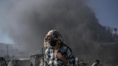 Bild: Petros Giannakouris/dpa
Eine Frau mit Mund- und Kopfbedeckung geht vor einer große Rauchwolke über dem Flüchtlingslager Moria weg. Das Flüchtlingslager ist durch einen Großbrand in der Nacht nahezu vollständig zerstört worden.