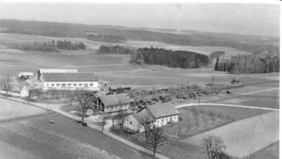 Bild: Bildarchiv der Gemeinde Ursensollen
Diese Luftaufnahme aus dem Jahr 1958 zeigt die damals noch "einsame Lage" des Bahnhofes Ursensollen und der beiden Lagerhäuser südlich des Ortskernes. Westlich der AS 4 findet sich nun das Edeka-Geschäft, südlich zum Beispiel die Firma KTM. Die Abzweigung zur AS 15 in Richtung Hohenkemnath verlief zu dieser Zeit noch mitten durch beide Lagerhausteile. Das Holzlager beim Bahnhof erinnert noch an die West-Erweiterung des Truppenübungsplatzes Hohenfels im Jahre 1951. Damals durften die abgelösten Bauern noch einige Monate in ihren Wäldern einen Holzabschlag durchführen, der Holzhändler aus ganz Deutschland anlockte. Im Hintergrund ist die ehemalige Halle der Firma Ehebauer zu sehen. Später war hier die Firma Schmieding. Nun - seit 2008 - ist hier die Firma "Dr. Dr. Eberth, Arzneimittel" angesiedelt.