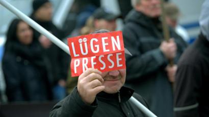 Archivbild: Paul Zinken/dpa
Ein Mann zeigt bei einer Demonstration eines rechtspopulistischen Bürgerbündnisses dem Fotografen ein Schild mit der Aufschrift „Lügenpresse“.