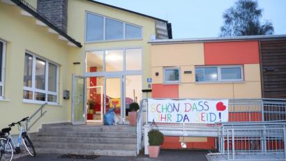 Bild: flt
Die Freude darüber, dass die Kinder zur Zeit den Kindergarten besuchen dürfen, drückten die Mitarbeiterinnen mit dem Transparent neben dem EIngang aus. Bei der Besichtigung erklärte Bürgermeister Müller den Räten, worum es in dem Antrag des Elternbeirats mit dem Vordach über dem Eingang ging, der allerdings nach vorheriger Absprache mit der Kindergartenleitung abgelehnt wurde.