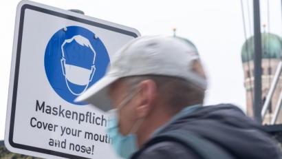 Bild: Peter Kneffel/dpa
Ein Passant geht an einem Schild vorbei, das auf das Tragen einer Maske hinweist.