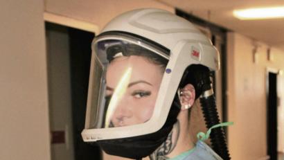 Bild: Marie Ehras/exb
Eine Pflegekraft mit Atemschutzhelm – diese Helme werden derzeit im St.-Anna-Krankenhaus getestet, anschließend wird über die Anschaffung für die Mitarbeiter im Isolations-Bereich und in der Notaufnahme entschieden. Ein Gebläsefilter auf dem Rücken sorgt dafür, dass ständig ein gereinigter, frischer Luftstrom vor das Gesicht des Trägers transportiert wird.