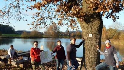 Bild: Portner
Der Weiher bei Muschenried ist auch im Herbst ein Naturjuwel. Anja Ried (rechts) und Johanna Bösl kleben die Markierung für den „W 3“-Weg an den Baumstamm. Ramona Griebl und Bürgermeisterin Sonja Meier (Mitte) präsentieren die Wanderkarte, und Lucie testet die Sitzbank.
