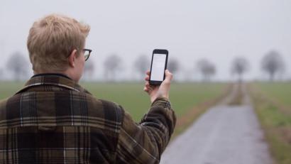 Bild: Julian Stratenschulte/dpa
Ein Mann lässt auf einem Feldweg sein Smartphone nach Netzbetreibern suchen (gestellte Szene).