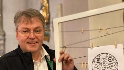 Bild: edo
Pater Adrian zeigt einen der 24 QR-Codes (rundes Symbol), die in den Kirchen der Pfarreien-Gemeinschaft zu finden sind. Für die technische Umsetzung war Schlammersdorfs zweite Bürgermeisterin Tanja Renner zuständig.