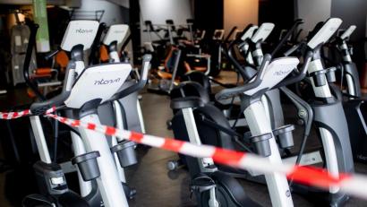 Bild: Hauke-Christian Dittrich/dpa
Ein rot-weißes Flatterband ist an Fahrradtrainern befestigt, die in einem Fitnessstudio stehen.