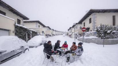 Bild: Bernat Armangue/AP/dpa
Nachbarn haben sich bei dichtem Schneefall mit Getränken in der Mitte einer Straße an einen Tisch gesetzt.